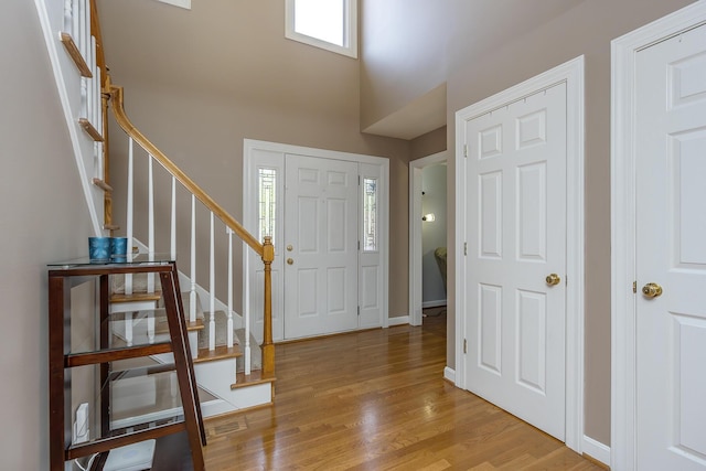 foyer entrance with stairway, wood finished floors, a towering ceiling, and baseboards