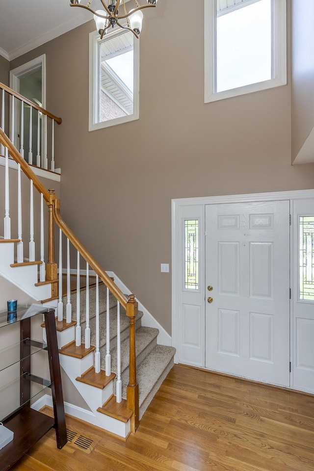 foyer entrance with a chandelier, stairs, wood finished floors, crown molding, and a high ceiling