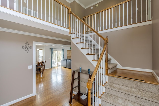 stairs featuring ornamental molding, wood finished floors, a high ceiling, and baseboards