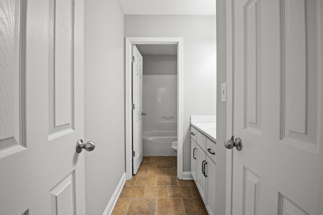 bathroom with baseboards, stone finish flooring, vanity, a bath, and toilet