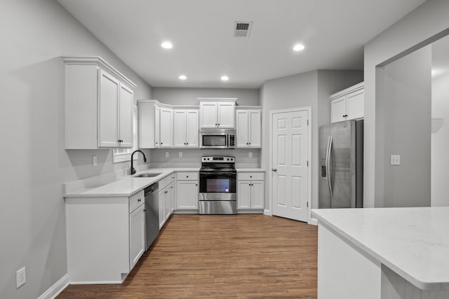 kitchen with appliances with stainless steel finishes, a sink, recessed lighting, wood finished floors, and white cabinetry