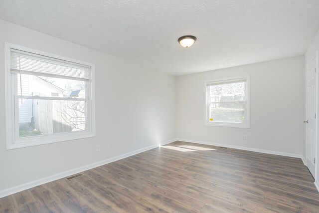 unfurnished room with healthy amount of natural light, dark wood finished floors, baseboards, and a textured ceiling