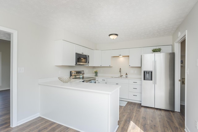 kitchen featuring stainless steel appliances, dark wood finished floors, light countertops, a sink, and a peninsula