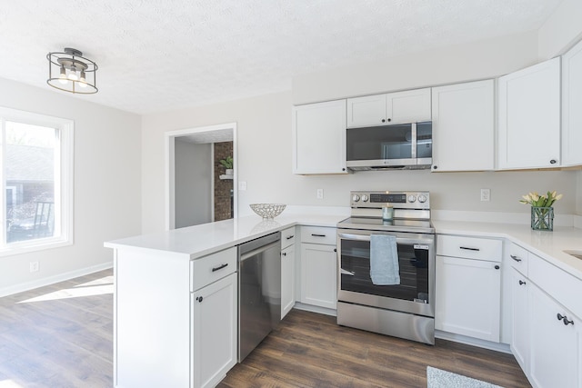 kitchen with stainless steel appliances, a peninsula, light countertops, white cabinets, and a textured ceiling