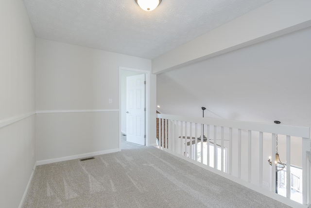 carpeted spare room featuring a textured ceiling and baseboards