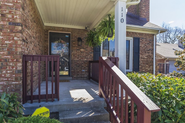 view of exterior entry with brick siding, a porch, and roof with shingles