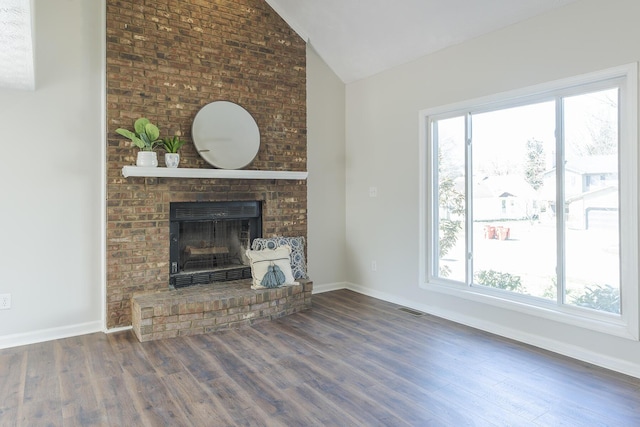 unfurnished living room with lofted ceiling, healthy amount of natural light, wood finished floors, a brick fireplace, and baseboards
