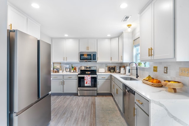 kitchen featuring stainless steel appliances, a sink, backsplash, light wood-type flooring, and recessed lighting