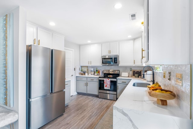 kitchen with appliances with stainless steel finishes, a sink, light wood-style floors, light stone countertops, and recessed lighting