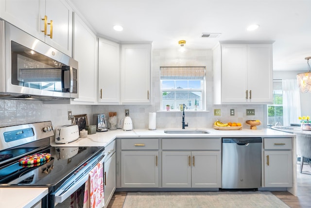 kitchen with stainless steel appliances, a sink, gray cabinetry, backsplash, and recessed lighting