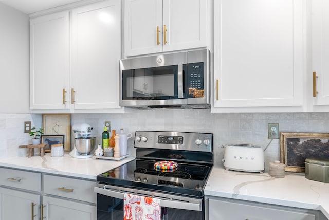 kitchen featuring appliances with stainless steel finishes, white cabinetry, tasteful backsplash, and light stone counters