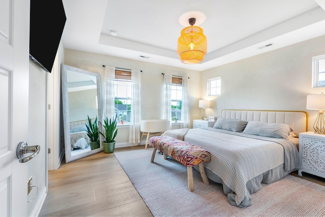 bedroom with light wood-style flooring, a raised ceiling, and baseboards