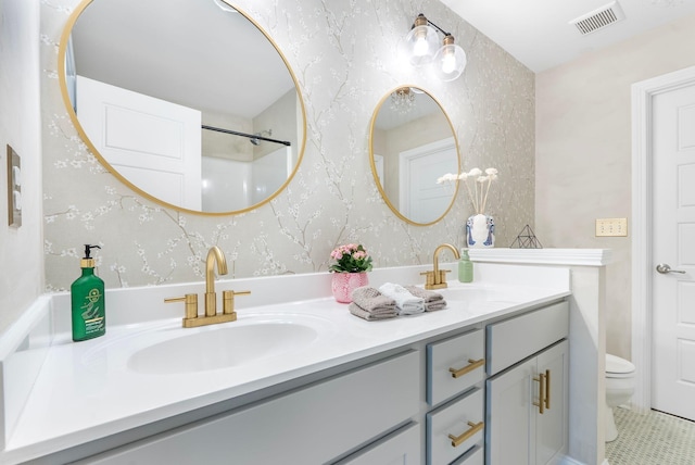 full bath featuring toilet, double vanity, and wallpapered walls