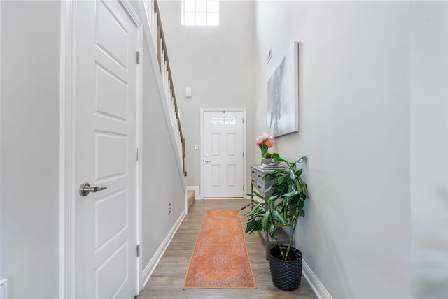 entryway with baseboards, light wood-style flooring, a towering ceiling, and stairway