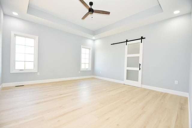 unfurnished room featuring a barn door, a tray ceiling, ceiling fan, light wood-style floors, and recessed lighting