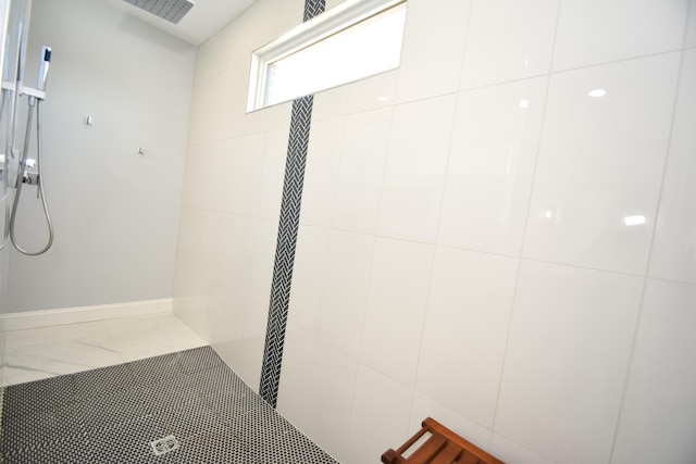 bathroom with a tile shower, marble finish floors, and baseboards