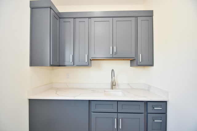 kitchen with gray cabinetry, light stone counters, and a sink