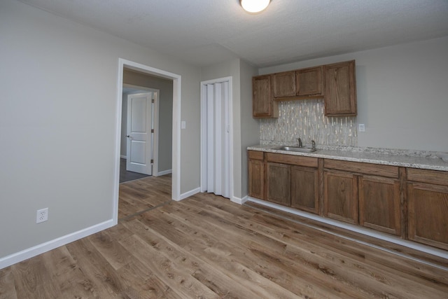 kitchen with a sink, light wood-style floors, backsplash, and brown cabinetry