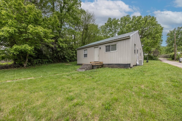 back of property with a lawn, metal roof, a cooling unit, and view of wooded area