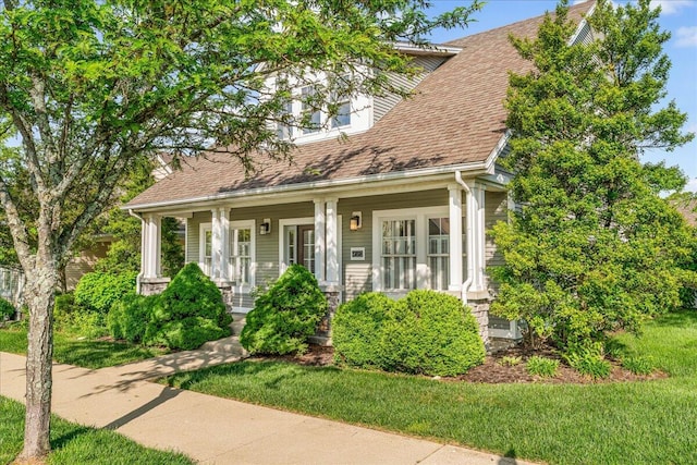 new england style home with covered porch, roof with shingles, and a front yard