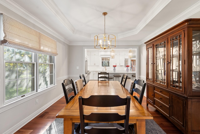 dining room featuring a chandelier, dark wood finished floors, a tray ceiling, and ornamental molding