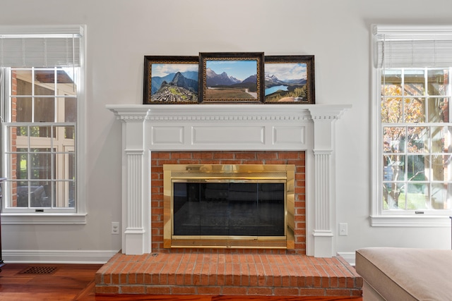 detailed view of baseboards, wood finished floors, and a brick fireplace