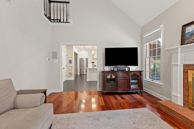 living area with baseboards, dark wood-style flooring, a brick fireplace, and high vaulted ceiling