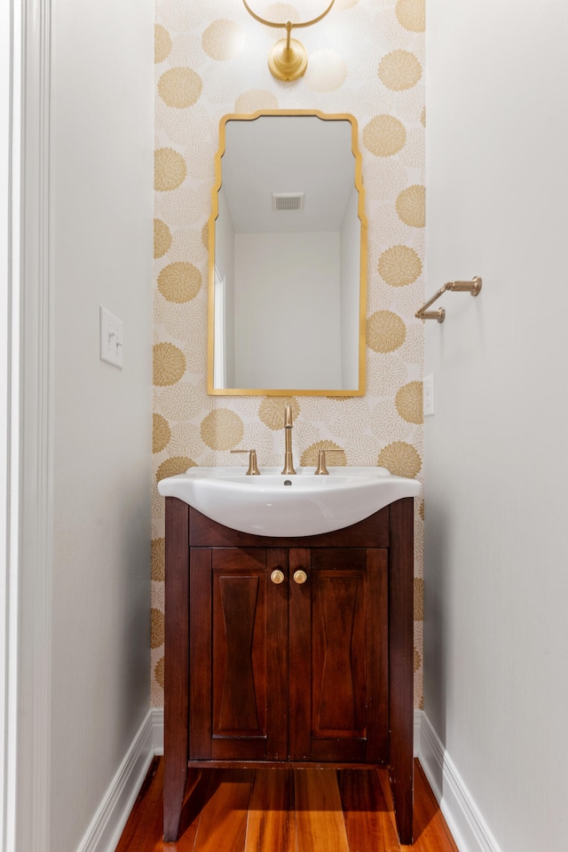 bathroom featuring wallpapered walls, wood finished floors, vanity, and baseboards