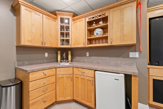 kitchen with a sink, refrigerator, light brown cabinetry, and glass insert cabinets