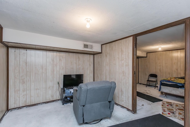 living area featuring wooden walls, unfinished concrete floors, and a textured ceiling