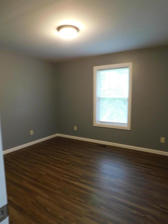 spare room featuring dark wood-style flooring and baseboards