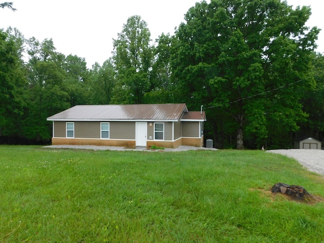 ranch-style home featuring a front yard, metal roof, an outdoor fire pit, and a storage unit