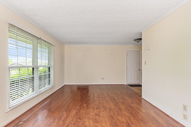 empty room with wood finished floors, crown molding, a textured ceiling, and baseboards