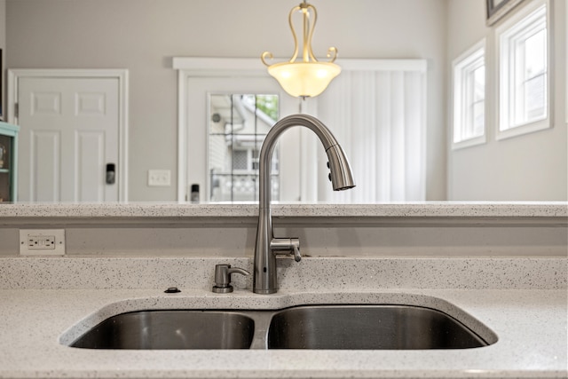 kitchen view of a sink, decorative light fixtures, and light stone counters