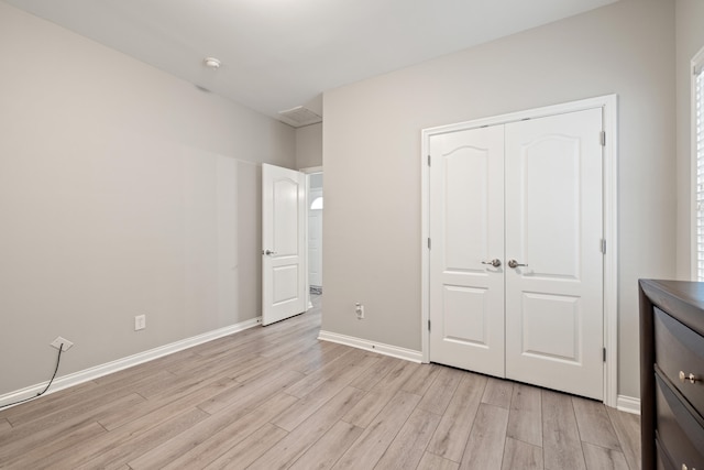 unfurnished bedroom featuring light wood-style floors, baseboards, and a closet