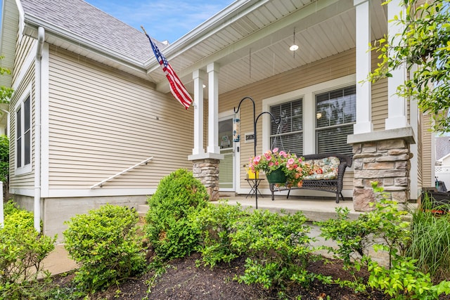 view of exterior entry featuring a porch, a shingled roof, and stone siding