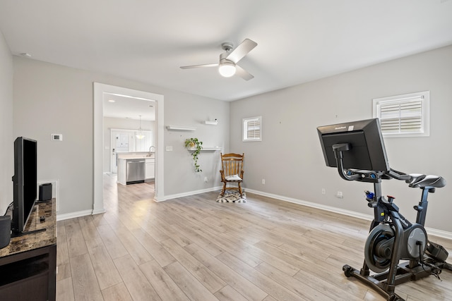 workout area featuring a ceiling fan, light wood-style flooring, baseboards, and a sink