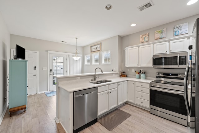 kitchen with appliances with stainless steel finishes, a sink, a peninsula, white cabinets, and light wood-type flooring