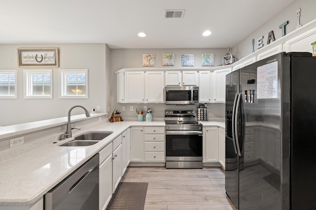 kitchen featuring appliances with stainless steel finishes, a sink, light wood-type flooring, white cabinets, and recessed lighting