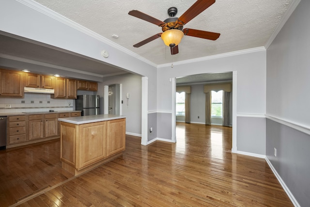 kitchen with appliances with stainless steel finishes, under cabinet range hood, wood-type flooring, light countertops, and a kitchen island