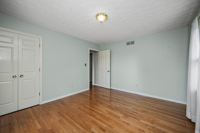 unfurnished bedroom with wood finished floors, baseboards, a textured ceiling, and a closet
