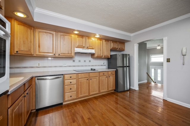 kitchen featuring appliances with stainless steel finishes, under cabinet range hood, dark wood finished floors, light countertops, and crown molding
