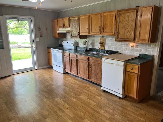 kitchen with white appliances, under cabinet range hood, brown cabinetry, tasteful backsplash, and crown molding