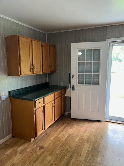 kitchen featuring light wood-style floors, brown cabinets, dark countertops, wood walls, and ornamental molding