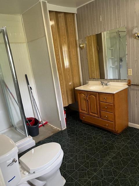 full bathroom featuring a stall shower, toilet, wooden walls, and vanity