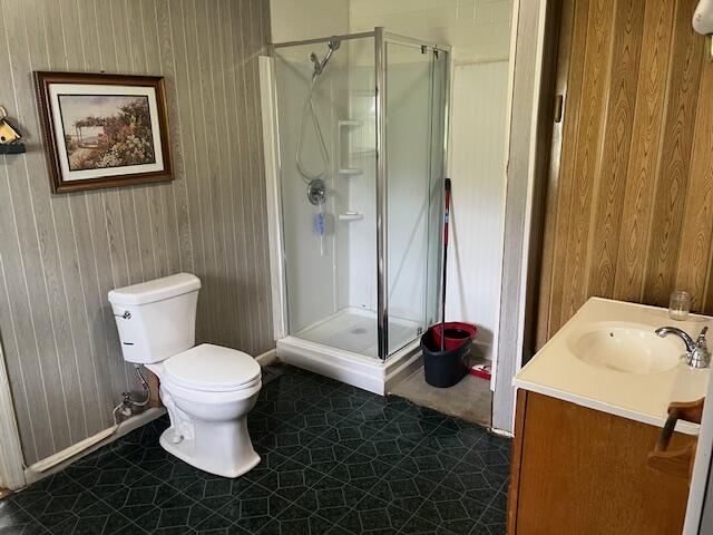 full bathroom with a shower stall, baseboards, toilet, and wooden walls