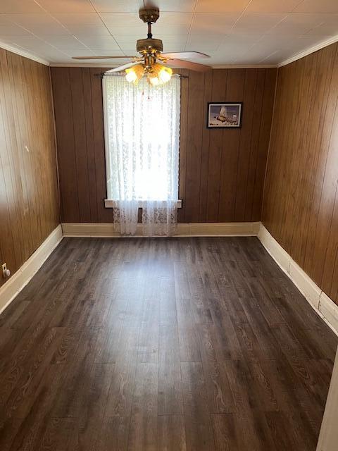 unfurnished dining area featuring a ceiling fan, dark wood finished floors, baseboards, and wooden walls