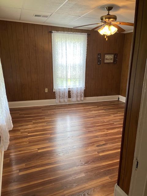 empty room with dark wood-style flooring, a ceiling fan, baseboards, and wooden walls