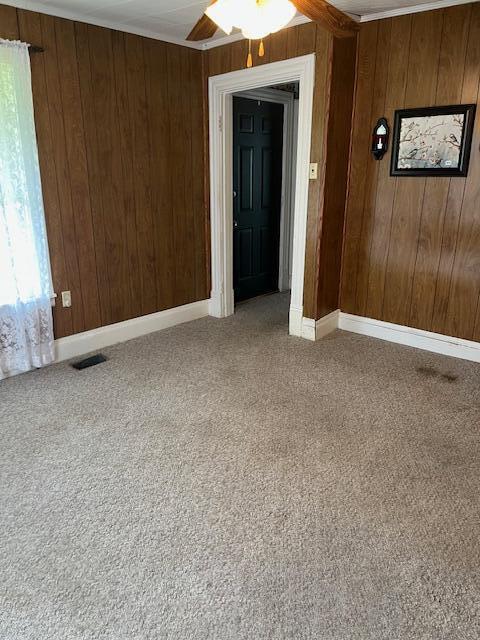 empty room with wood walls, light carpet, ceiling fan, baseboards, and crown molding