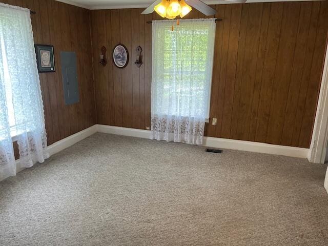 carpeted spare room featuring a ceiling fan, wooden walls, and baseboards